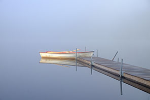 En båt ligger förankrad vid en brygga. Runtomkring är det dimma.