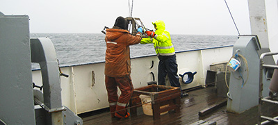 Två personer på båt som arbetar med provgtagningsutrustning.